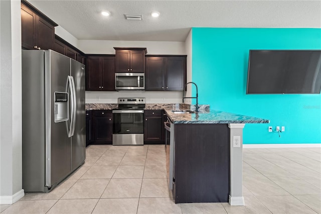 3762 Mossy Limb Ct, Palmetto, FL 34221 - kitchen featuring appliances with stainless steel finishes, dark stone countertops, dark brown cabinets, a peninsula, and light tile patterned floors