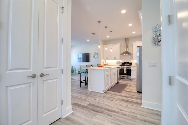 803 Oak Bend Ln, Dunedin, FL 34698 - kitchen featuring appliances with stainless steel finishes, wall chimney range hood, a breakfast bar area, white cabinetry, and light wood-type flooring