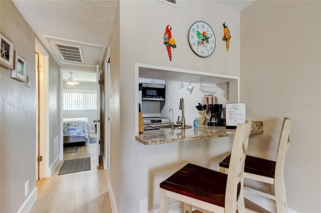 282 Treasure Island Cswy Unit 12, Treasure Island, FL 33706 - kitchen featuring appliances with stainless steel finishes, wood finished floors, a breakfast bar area, stone counters, and a ceiling fan