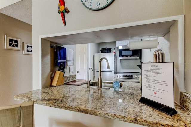 282 Treasure Island Cswy Unit 12, Treasure Island, FL 33706 - kitchen with stainless steel appliances, light stone countertops, a peninsula, and white cabinetry
