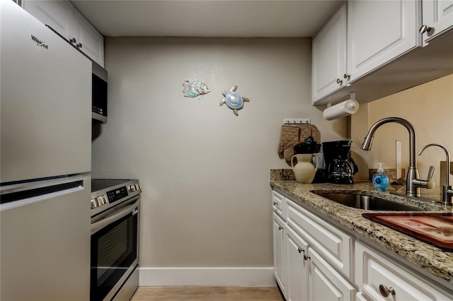 282 Treasure Island Cswy Unit 12, Treasure Island, FL 33706 - kitchen featuring appliances with stainless steel finishes, light stone counters, white cabinets, and light wood-style floors