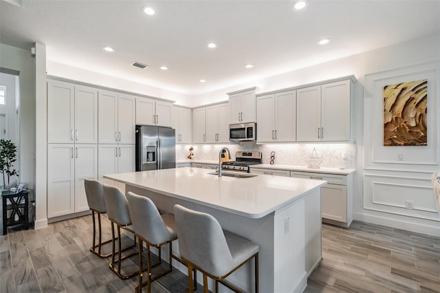 3197 Acacia Bay Ave, Wesley Chapel, FL 33543 - kitchen featuring appliances with stainless steel finishes, a breakfast bar, a kitchen island with sink, light wood-style flooring, and recessed lighting