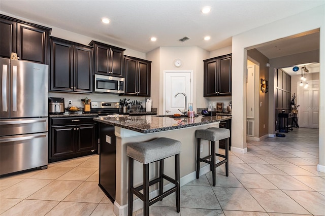 11711 Winterset Cove Dr, Riverview, FL 33579 - kitchen featuring appliances with stainless steel finishes, dark stone countertops, a kitchen breakfast bar, light tile patterned flooring, and a center island with sink