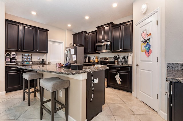11711 Winterset Cove Dr, Riverview, FL 33579 - kitchen featuring stainless steel appliances, light tile patterned flooring, a breakfast bar, an island with sink, and dark stone countertops