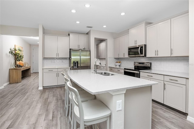 8423 Praise Dr, Tampa, FL 33625 - kitchen featuring appliances with stainless steel finishes, a sink, light wood-style floors, an island with sink, and backsplash