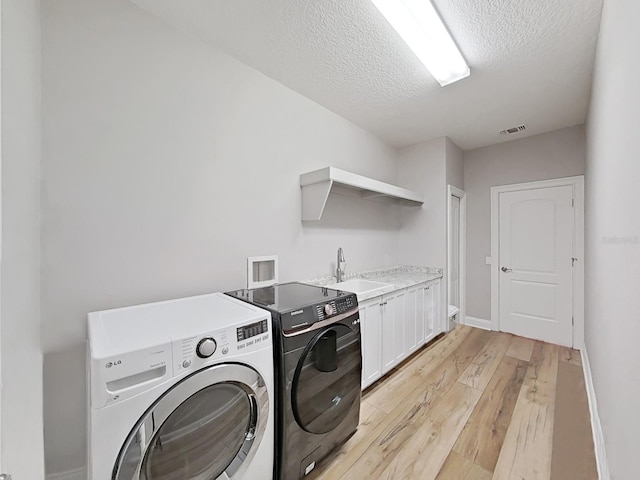 15024 Eaglepark Pl, Lithia, FL 33547 - laundry area featuring light wood finished floors, washer and dryer, cabinet space, and a textured ceiling