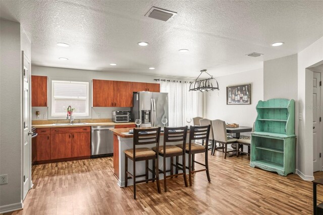 630 Mac Crillus Rd, Largo, FL 33770 - kitchen with stainless steel appliances, light wood-style flooring, a textured ceiling, brown cabinetry, and a kitchen bar