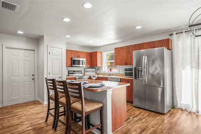 630 Mac Crillus Rd, Largo, FL 33770 - kitchen featuring appliances with stainless steel finishes, brown cabinetry, light wood-style flooring, recessed lighting, and a textured ceiling