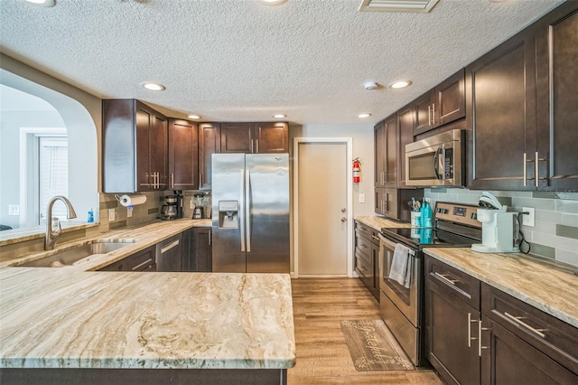 51 Cypress Dr, Palm Harbor, FL 34684 - kitchen featuring stainless steel appliances, dark brown cabinetry, light wood-style flooring, backsplash, and a textured ceiling
