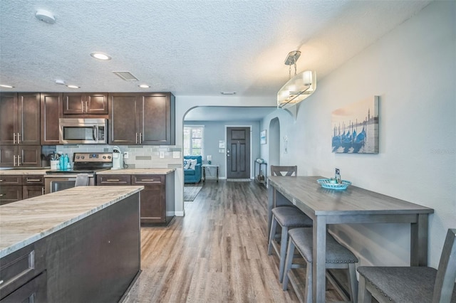 51 Cypress Dr, Palm Harbor, FL 34684 - kitchen with stainless steel appliances, arched walkways, light wood-type flooring, dark brown cabinetry, and backsplash