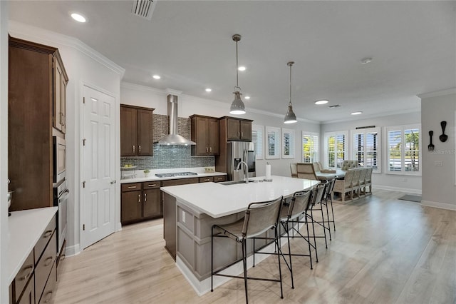 7420 Paradiso Dr, Apollo Beach, FL 33572 - kitchen with wall chimney range hood, appliances with stainless steel finishes, a kitchen island with sink, a breakfast bar, and light wood-style floors