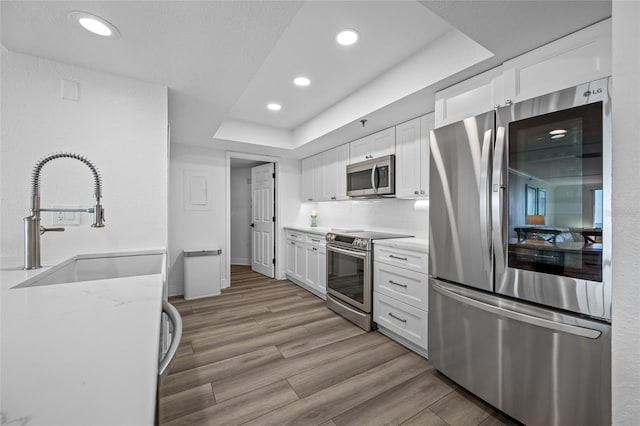 6372 Palma Del Mar Blvd S Unit 601, Saint Petersburg, FL 33715 - kitchen featuring appliances with stainless steel finishes, white cabinets, a raised ceiling, recessed lighting, and light wood-type flooring