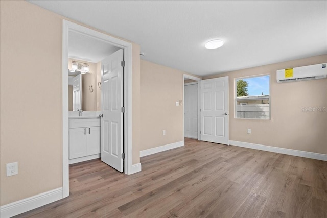 21536 Holdern Ave, Port Charlotte, FL 33952 - unfurnished bedroom with an AC wall unit, light wood finished floors, baseboards, a sink, and ensuite bath