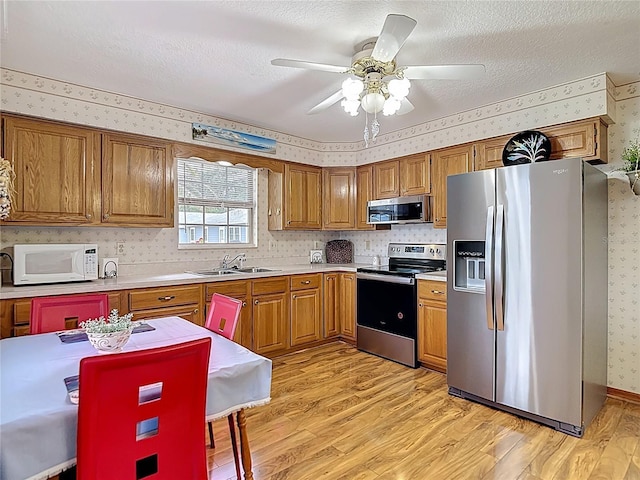 5755 Yorkshire Dr, Zephyrhills, FL 33542 - kitchen featuring stainless steel appliances, wallpapered walls, light wood-style floors, brown cabinets, and light countertops