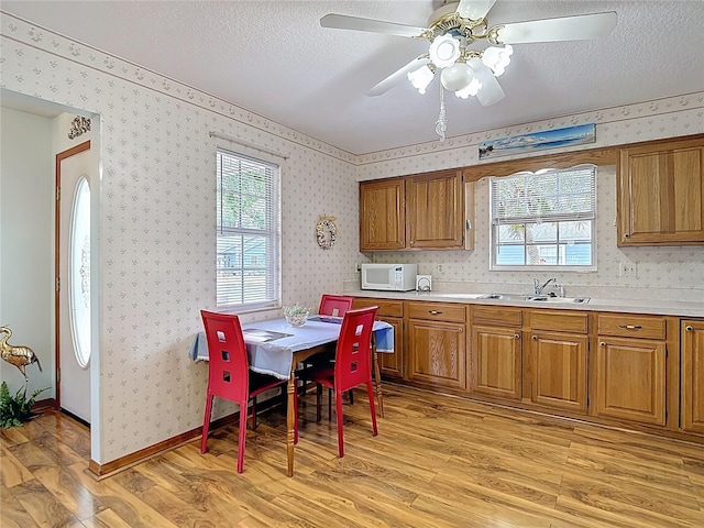5755 Yorkshire Dr, Zephyrhills, FL 33542 - kitchen featuring white microwave, brown cabinets, light wood-type flooring, wallpapered walls, and light countertops