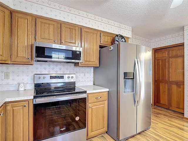 5755 Yorkshire Dr, Zephyrhills, FL 33542 - kitchen featuring stainless steel appliances, wallpapered walls, light countertops, light wood-style flooring, and a textured ceiling