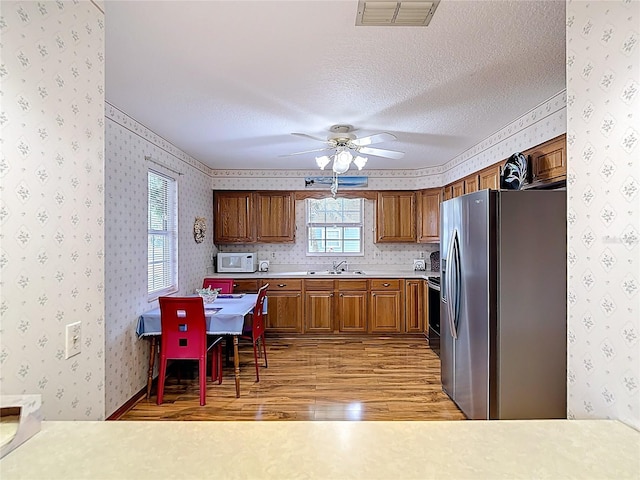 5755 Yorkshire Dr, Zephyrhills, FL 33542 - kitchen featuring stainless steel fridge with ice dispenser, wallpapered walls, light wood-style floors, brown cabinetry, and white microwave