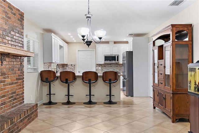 11029 Clay Pit Rd, Tampa, FL 33610 - kitchen with stainless steel appliances, a peninsula, tasteful backsplash, white cabinets, and a kitchen bar