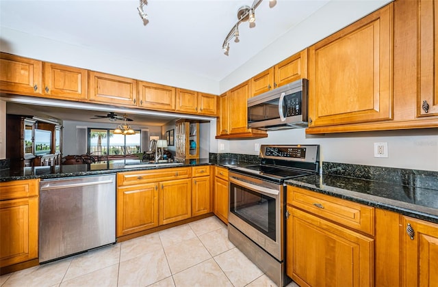 4450 Gulf Blvd Unit 110, St Pete Beach, FL 33706 - kitchen with stainless steel appliances, brown cabinets, light tile patterned floors, dark stone counters, and ceiling fan