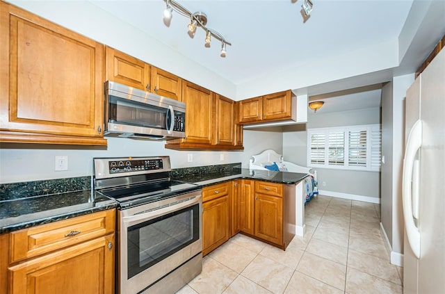 4450 Gulf Blvd Unit 110, St Pete Beach, FL 33706 - kitchen with appliances with stainless steel finishes, dark stone countertops, brown cabinetry, light tile patterned floors, and a peninsula