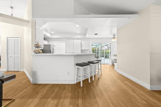 6051 65th Ave N, Pinellas Park, FL 33781 - kitchen with freestanding refrigerator, ceiling fan, a tray ceiling, light wood-style floors, and white cabinetry