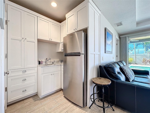 1204 Derby Ln, Sarasota, FL 34242 - kitchen featuring freestanding refrigerator, a sink, white cabinets, open floor plan, and a textured ceiling