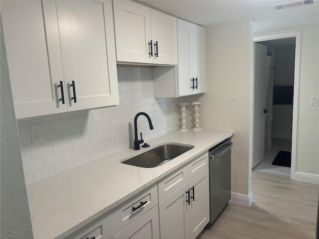 3640 41st Ln S Unit F, Saint Petersburg, FL 33711 - kitchen featuring stainless steel dishwasher, light wood finished floors, white cabinets, decorative backsplash, and light stone counters
