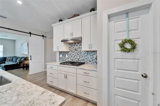 7116 Estero Ct, Apollo Beach, FL 33572 - kitchen with stainless steel gas stovetop, under cabinet range hood, light wood finished floors, decorative backsplash, and white cabinetry