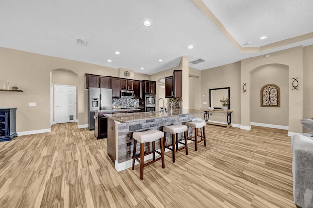 32624 Summerglade Dr, Wesley Chapel, FL 33545 - kitchen with arched walkways, appliances with stainless steel finishes, a breakfast bar, dark brown cabinetry, and recessed lighting