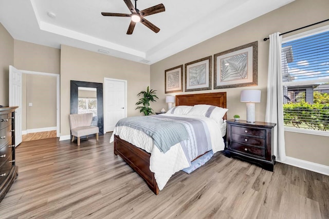 32624 Summerglade Dr, Wesley Chapel, FL 33545 - bedroom with light wood finished floors, multiple windows, a tray ceiling, and a ceiling fan