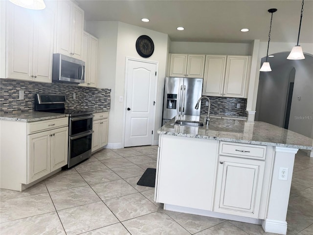 5082 Inshore Landings Dr, Apollo Beach, FL 33572 - kitchen featuring appliances with stainless steel finishes, backsplash, light stone countertops, hanging light fixtures, and a kitchen island with sink