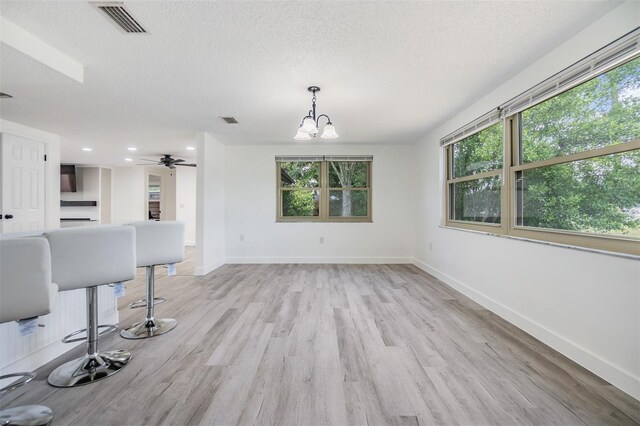 4228 Belle Isle Ct, New Port Richey, FL 34653 - unfurnished living room with a chandelier, a textured ceiling, light wood finished floors, healthy amount of natural light, and ceiling fan