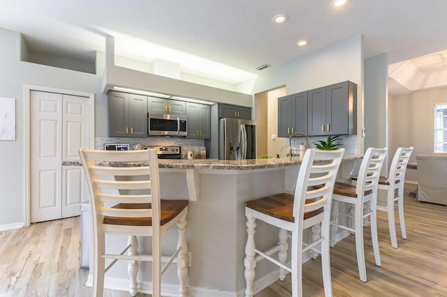 7725 235th St E, Myakka City, FL 34251 - kitchen with stainless steel appliances, light stone counters, decorative backsplash, light wood-type flooring, and a breakfast bar area