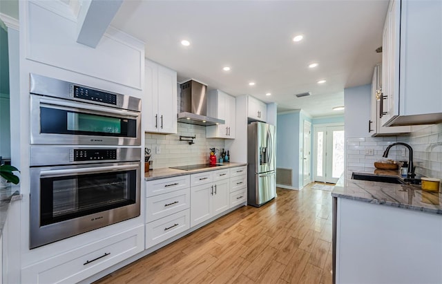 14534 Yacht Club Blvd, Seminole, FL 33776 - kitchen featuring wall chimney range hood, stainless steel appliances, decorative backsplash, light wood-style flooring, and white cabinetry
