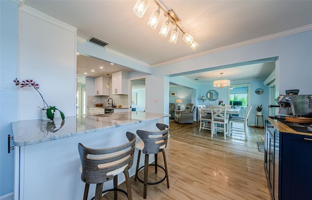 14534 Yacht Club Blvd, Seminole, FL 33776 - kitchen with crown molding, light wood-style floors, light stone countertops, backsplash, and a breakfast bar