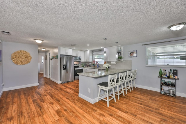 540 Firefly Ln, Apollo Beach, FL 33572 - kitchen with appliances with stainless steel finishes, a peninsula, dark wood-style floors, a breakfast bar area, and a textured ceiling