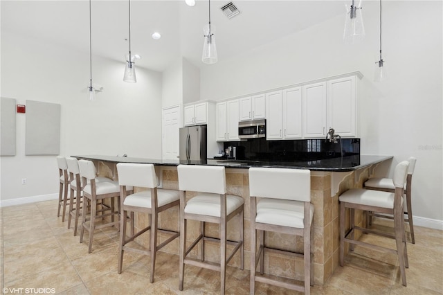 19781 Marino Lake Cir Unit 202, Miromar Lakes, FL 33913 - kitchen featuring appliances with stainless steel finishes, a towering ceiling, white cabinets, tasteful backsplash, and a breakfast bar