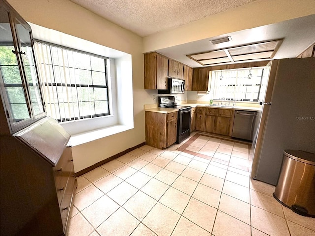 6262 E Rector St, Inverness, FL 34452 - kitchen with appliances with stainless steel finishes, brown cabinets, light countertops, light tile patterned flooring, and a textured ceiling