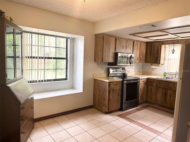 6262 E Rector St, Inverness, FL 34452 - kitchen featuring stainless steel appliances, light countertops, a textured ceiling, light tile patterned floors, and brown cabinets