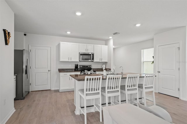 10823 Trailing Vine Dr, Tampa, FL 33610 - kitchen featuring stainless steel appliances, light wood-style flooring, white cabinets, a kitchen breakfast bar, and a kitchen island with sink