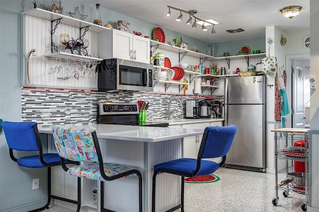 505 67th Ave Unit 11, St Pete Beach, FL 33706 - kitchen with open shelves, appliances with stainless steel finishes, backsplash, a kitchen bar, and dark aggregate flooring
