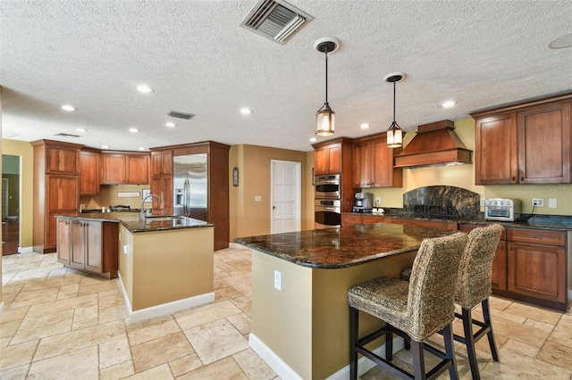 16205 Sentry Woods Ct, Odessa, FL 33556 - kitchen with premium range hood, a kitchen island with sink, appliances with stainless steel finishes, stone tile floors, and recessed lighting