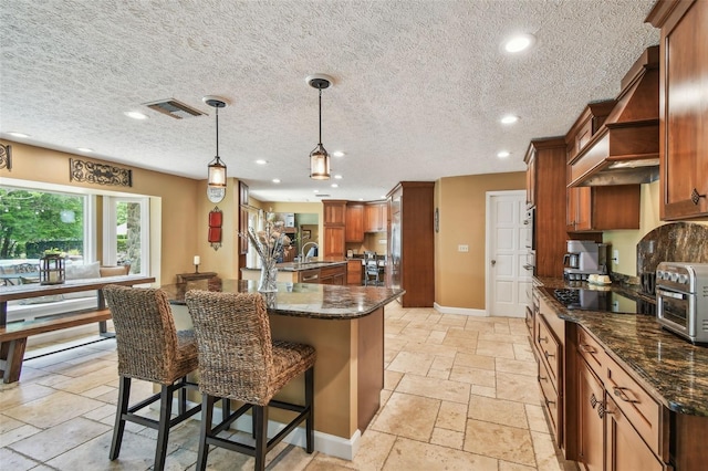 16205 Sentry Woods Ct, Odessa, FL 33556 - kitchen with premium range hood, stone tile floors, brown cabinetry, a center island with sink, and recessed lighting