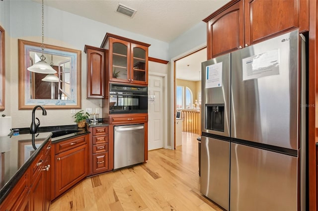 6543 Louise Ct, Hudson, FL 34667 - kitchen featuring stainless steel appliances, light wood finished floors, glass insert cabinets, hanging light fixtures, and dark stone countertops