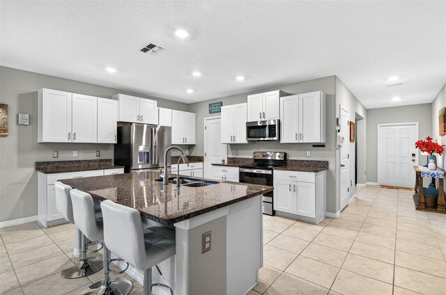 12835 Wildflower Meadow Dr, Riverview, FL 33579 - kitchen featuring stainless steel appliances, white cabinetry, light tile patterned floors, dark stone counters, and an island with sink