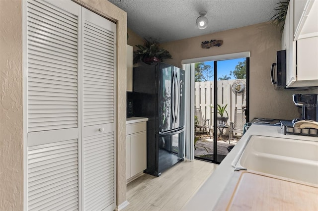 2922 60th St W, Bradenton, FL 34209 - kitchen with black appliances, a textured wall, a textured ceiling, light countertops, and light wood-style flooring