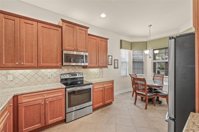 4911 Rock Island Ct, Wimauma, FL 33598 - kitchen with stainless steel appliances, decorative backsplash, brown cabinets, light tile patterned flooring, and hanging light fixtures