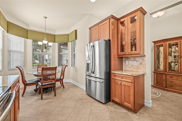 4911 Rock Island Ct, Wimauma, FL 33598 - kitchen featuring stainless steel appliances, brown cabinets, a chandelier, light tile patterned floors, and light stone counters