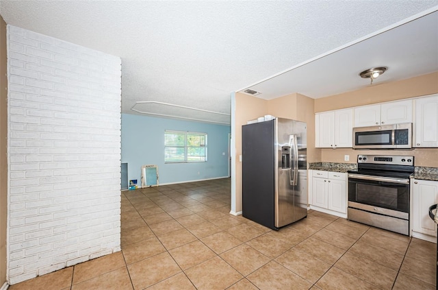 2003 Whispering Pines St, Largo, FL 33774 - kitchen featuring stainless steel appliances, light tile patterned floors, white cabinets, a textured ceiling, and dark stone countertops