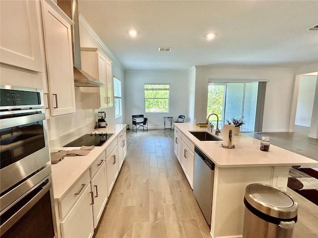 10864 Banyan Breeze Blvd, Land O Lakes, FL 34638 - kitchen featuring stainless steel appliances, light wood-style flooring, light countertops, wall chimney range hood, and white cabinets